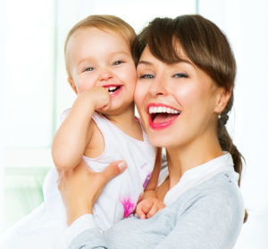 Mother holding baby both laughing with white smiles